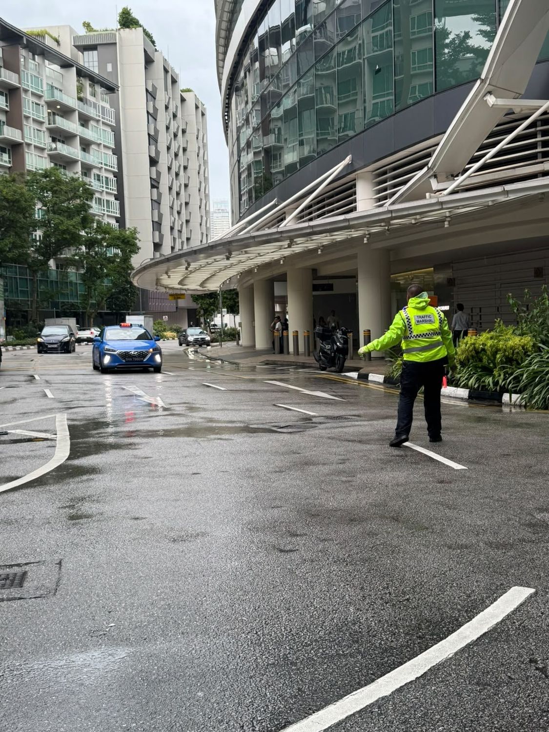 A Hawkeye traffic marshal in a hi-visibility vest directing vehicles at a Singapore hotel driveway
