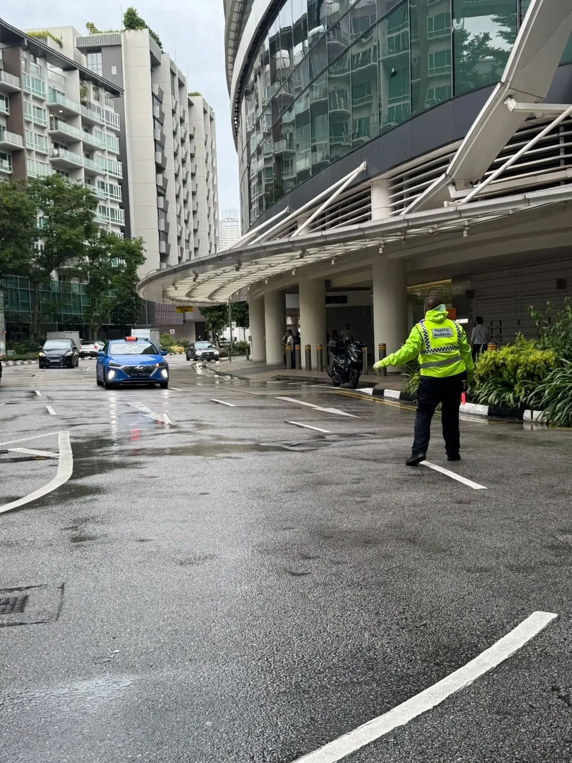 A Hawkeye traffic marshal in a hi-visibility vest directing vehicles at a Singapore hotel driveway